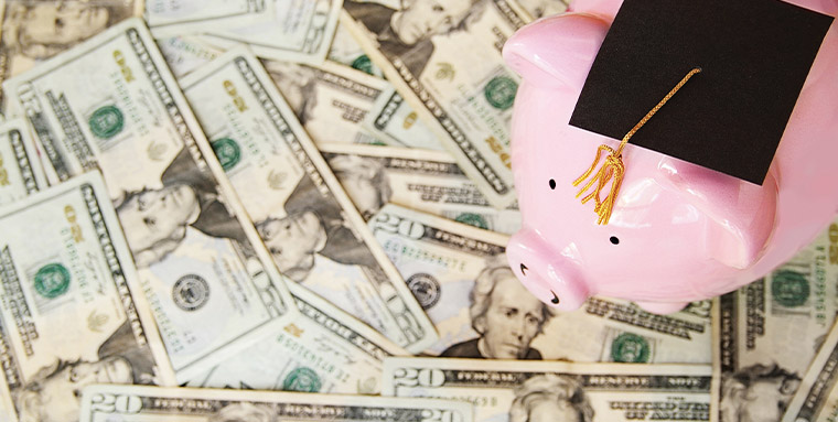 Piggybank with a grad cap standing on top of a pile of $20 dollar bills.