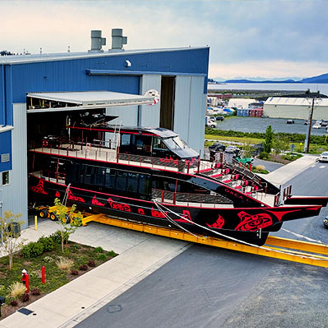 An enormous ship emerges from the All American Marine facility in Bellingham, Washington. The ship is painted black and decorated with red Coast Salish symbols.
