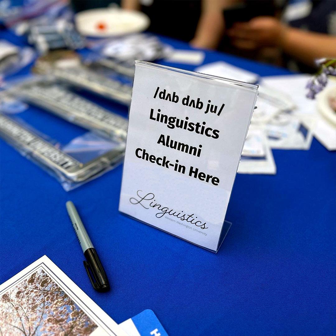 Event check-in table with navy blue cloth and a sign for Linguistics Alumni.