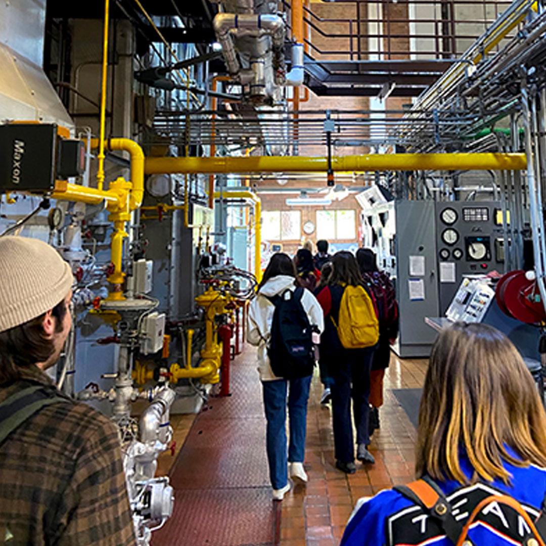 WWU students walk through a maze of colored pipes and large equipment in the university's steam plant.