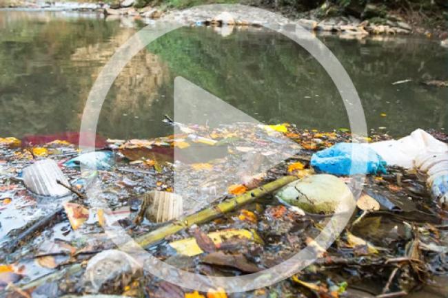 Very polluted river with a lot of trash floating in it with a video play button over it